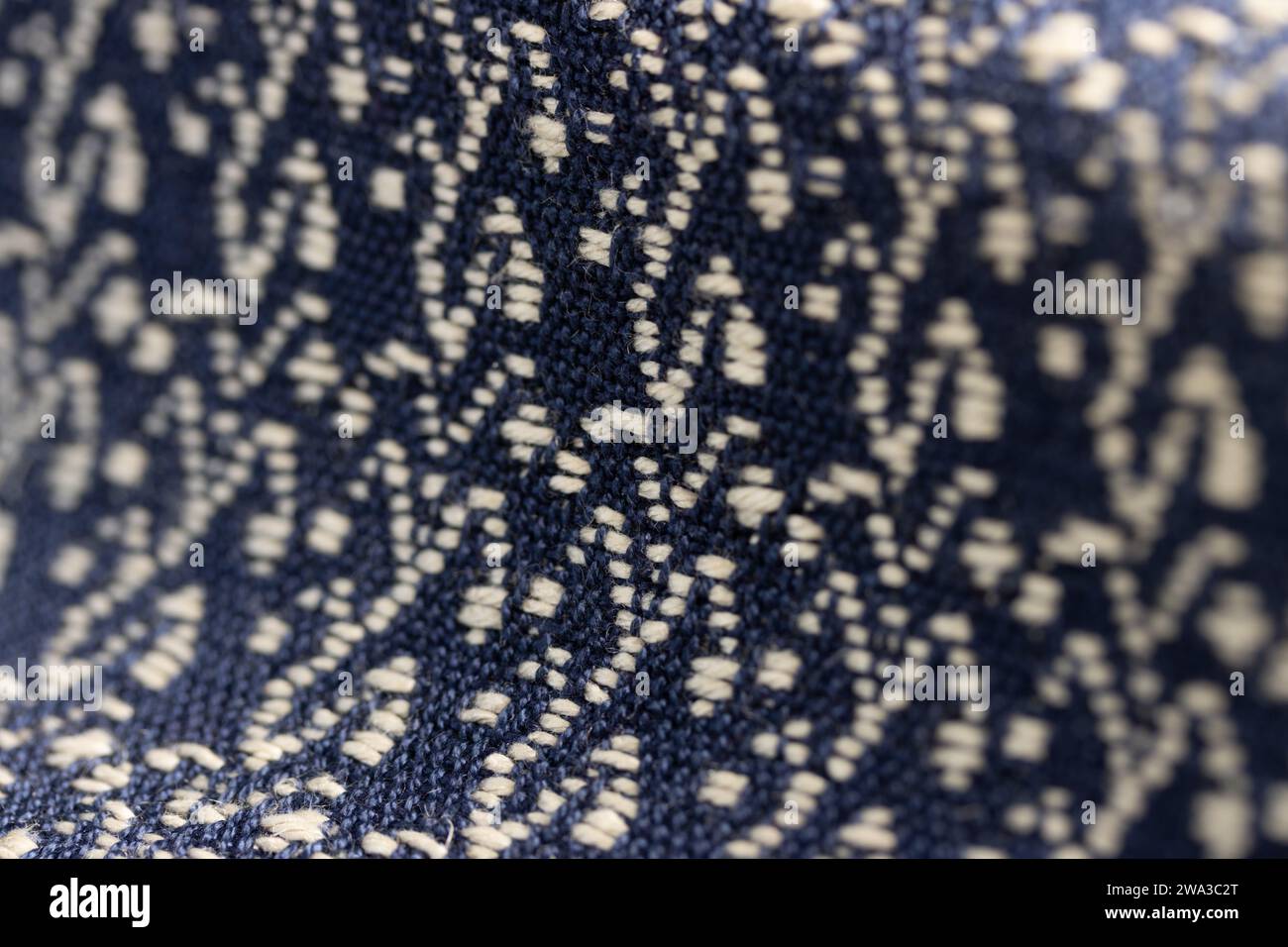 draped woven cloth with deep navy blue background and a cream white decorative pattern, close up macro detail shot of fibers with shallow depth of fie Stock Photo