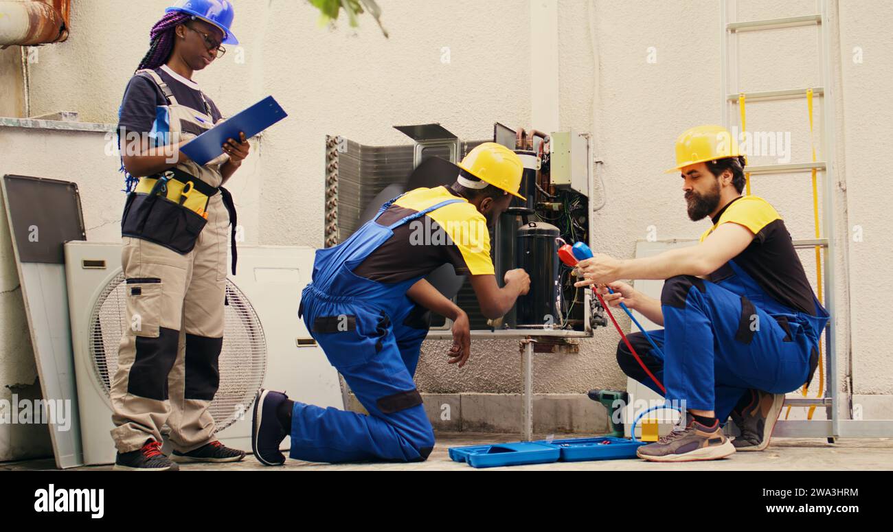 Competent mechanic cleaning layer of dirt and dust from condenser compressor coils while coworker uses measurement device to check for refrigerant leaks and read pressure in hvac system Stock Photo