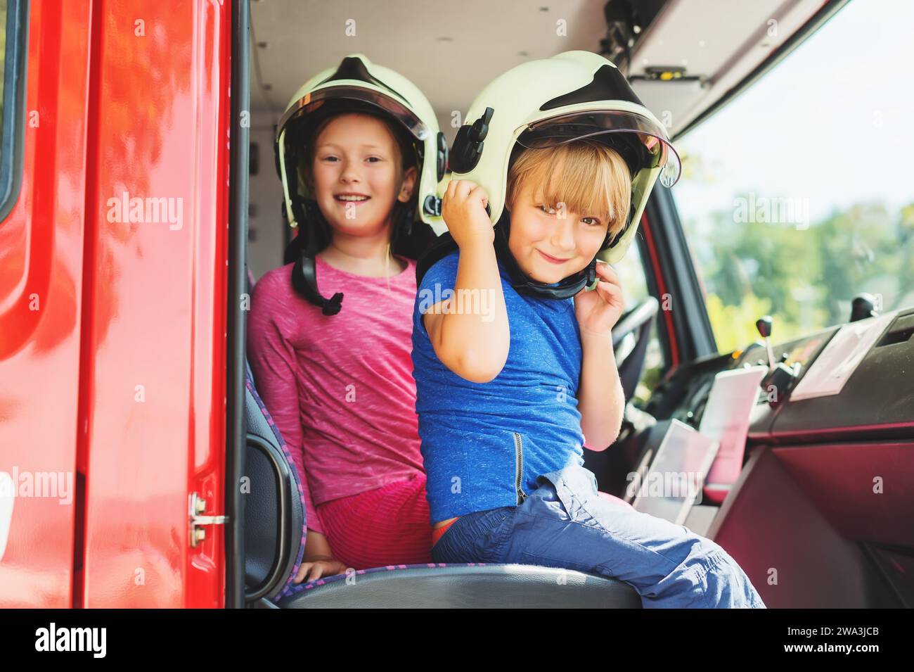 Two cute kids playing in fire truck, pretending to be firefighters, open doors day at fire station. Future profession for children. Educational progra Stock Photo