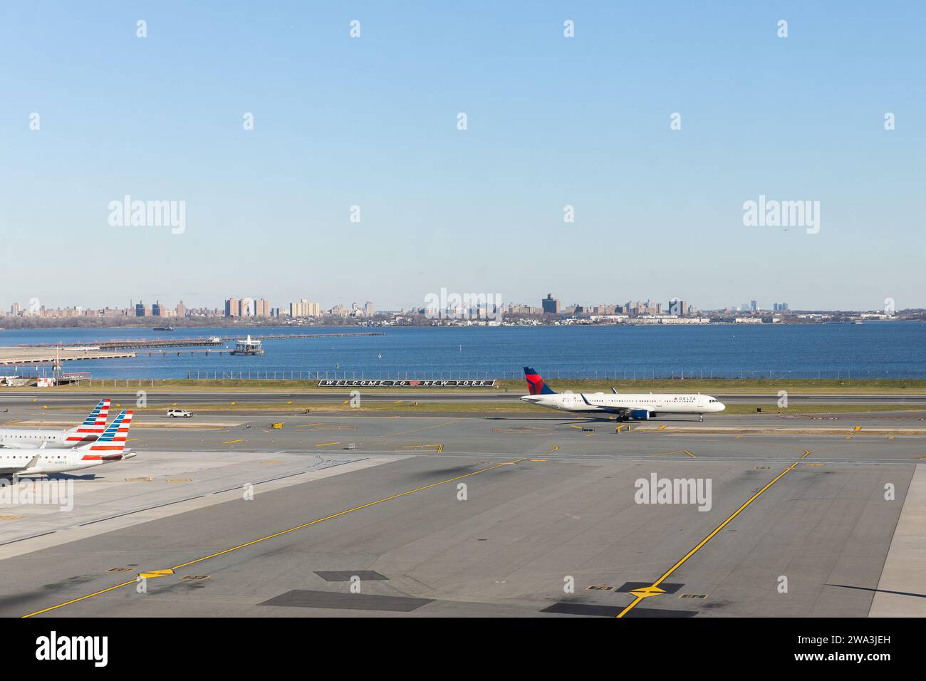 The LaGuardia Airport runway with a 'Welcome to New York' sign and a Delta Airlines plane taking off. Stock Photo