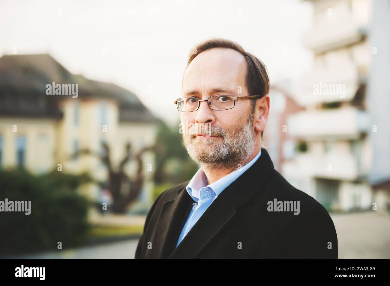 Outdoor portrait of 50 year old man wearing black coat and eyeglasses