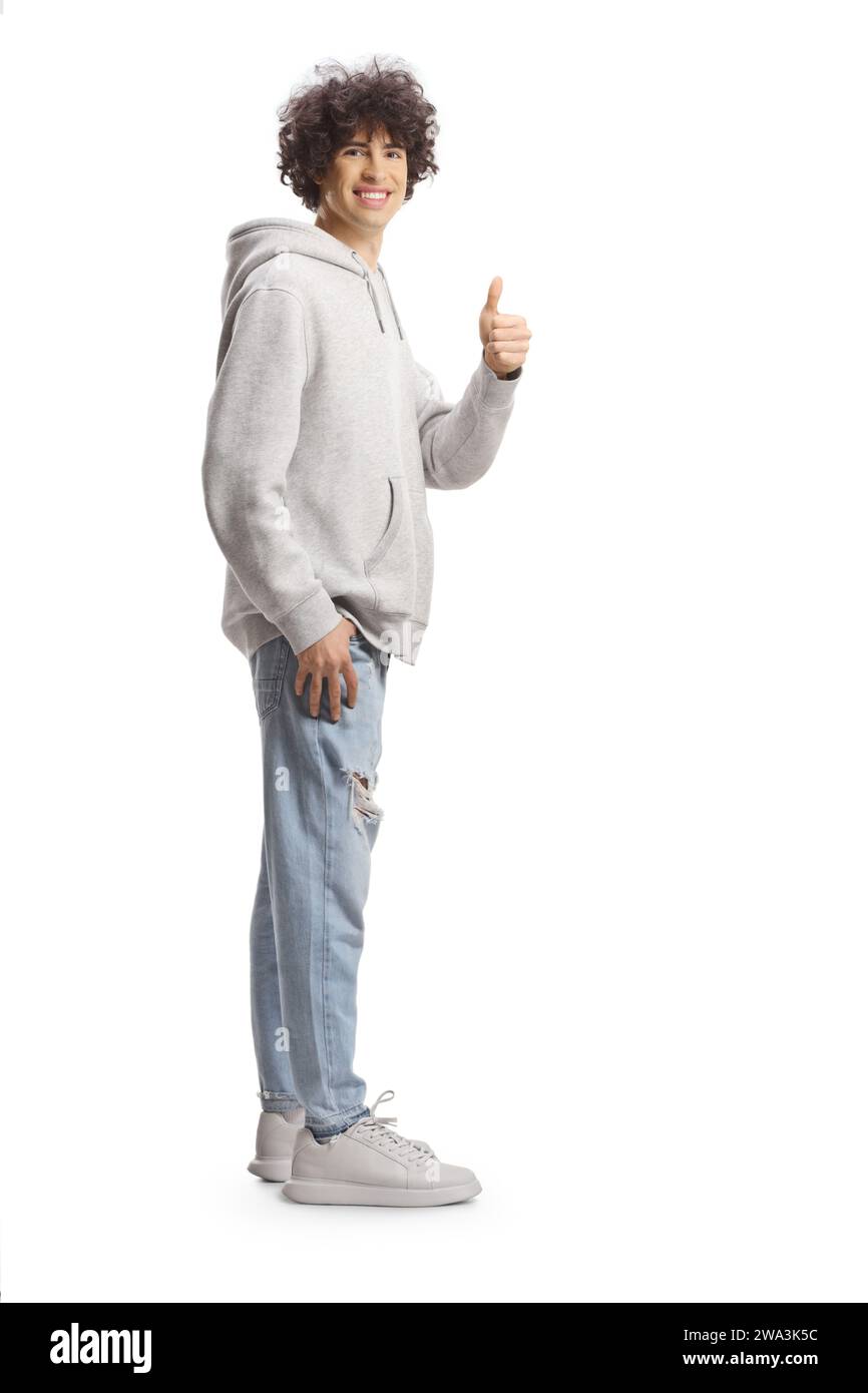 Full length portrait of a tall guy with curly hair in a gray hoodie and jeans gesturing thumbs up isolated on white background Stock Photo