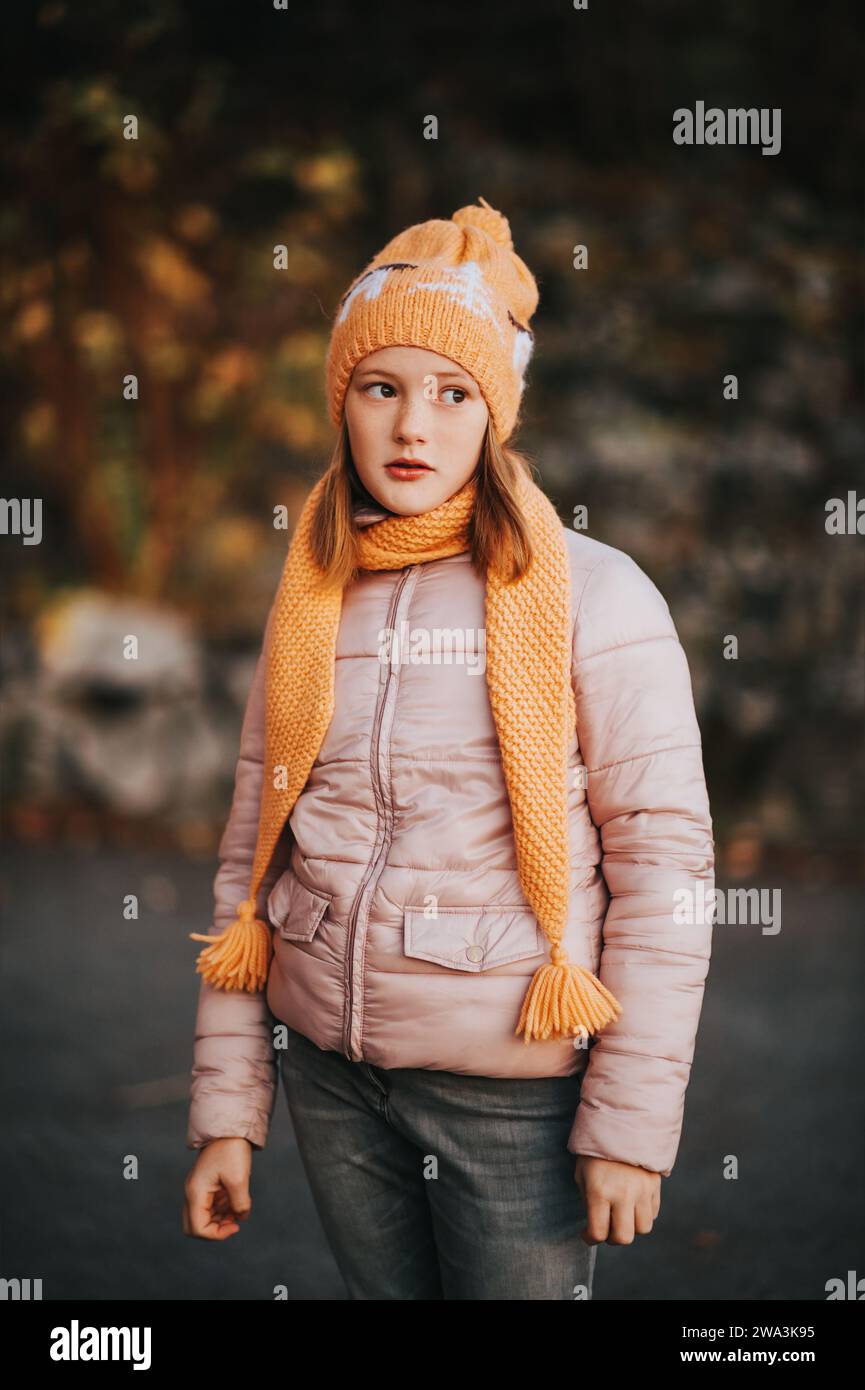 Outdoor portrait of pretty 10 year old girl wearing pink jacket and set of knitted hat and scarf Stock Photo