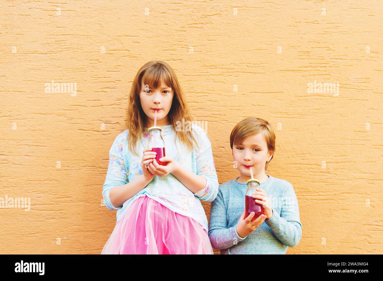 Outdoor portrait of two funny fashion kids, holding drinks, wearing blue and pink clothes Stock Photo