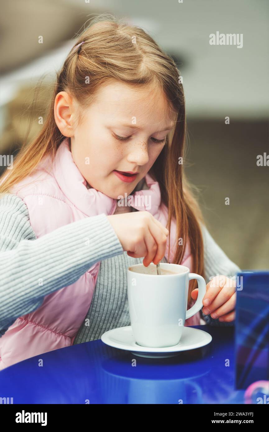 Outdoor portrait of a cute little girl drinking hot chocolate in a cafe Stock Photo