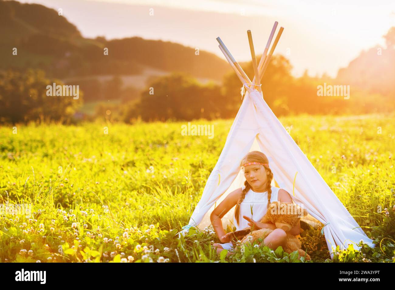 Happy kid girl sitting in a tent on a nice warm evening, playing drum music. Stock Photo