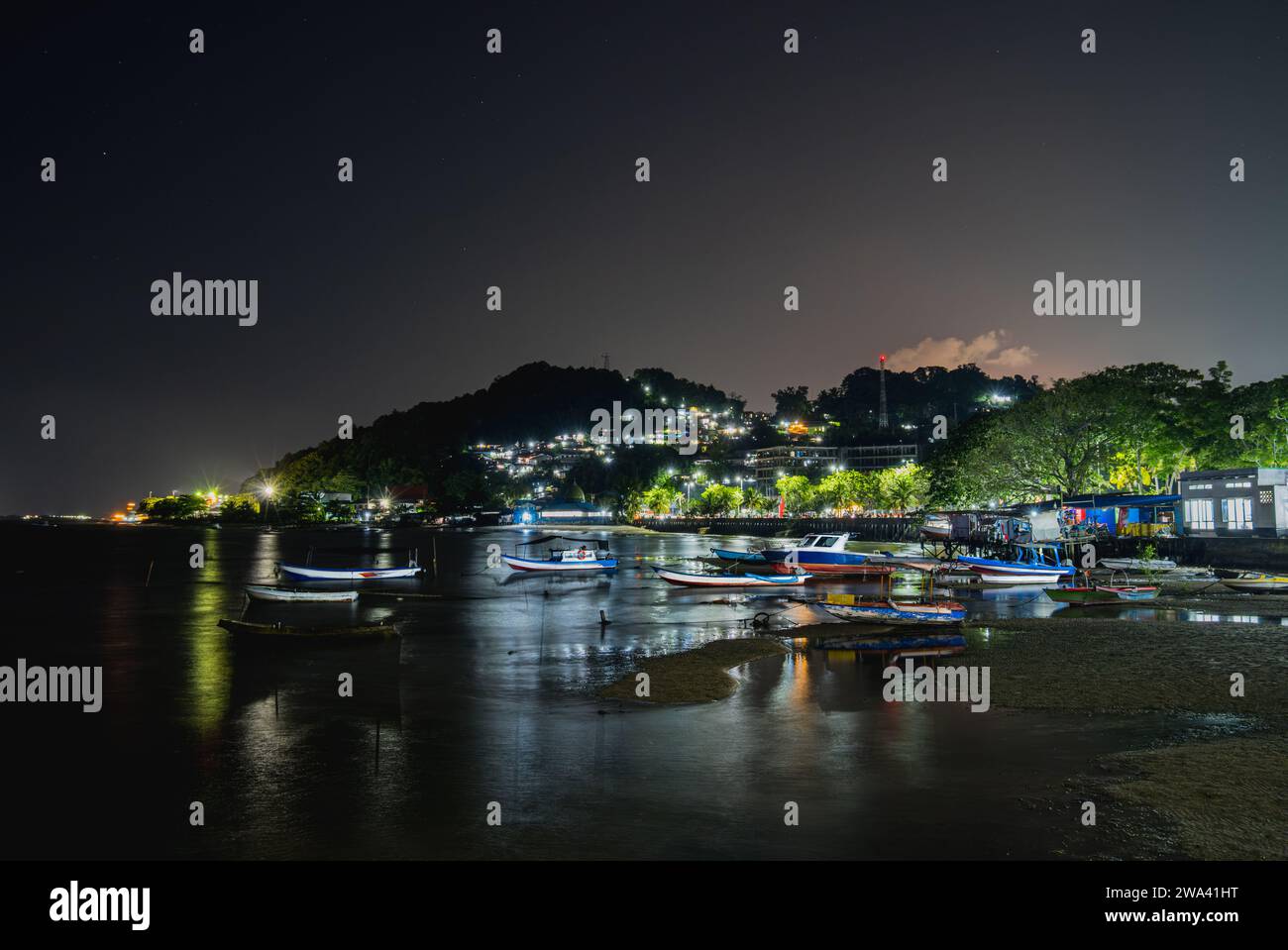 Fishermen boats resting at the shoreline in the night. and there are some fishing village stacked on the hill. Stock Photo