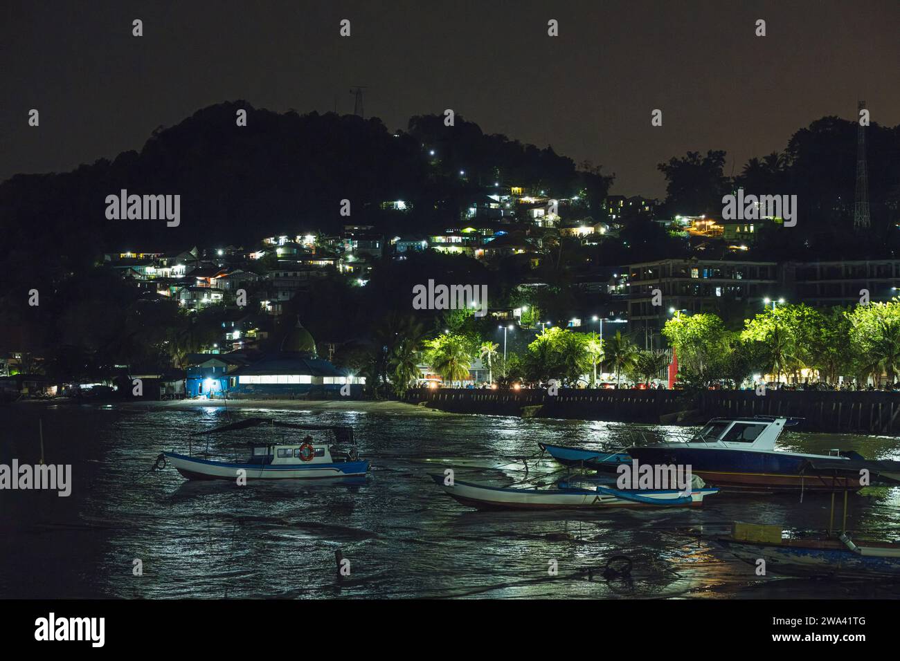 Fishermen boats resting at the shoreline in the night. and there are some fishing village stacked on the hill. Stock Photo