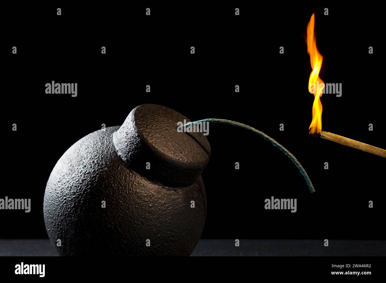 A matching lighting fuse of an old vintage round cast iron fragmentation bomb against a black