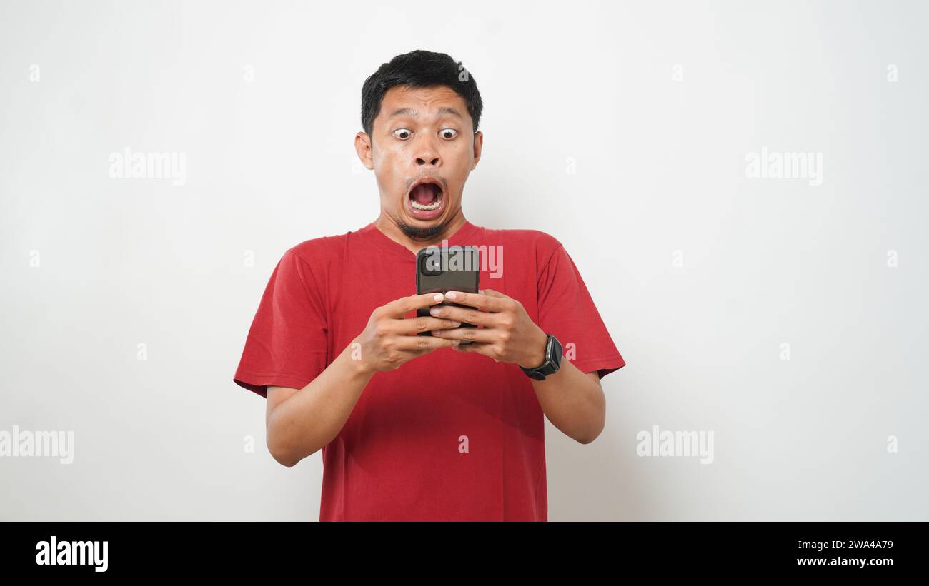 Wow face of Asian man shocked what he see in the smartphone on isolated grey background. Stock Photo