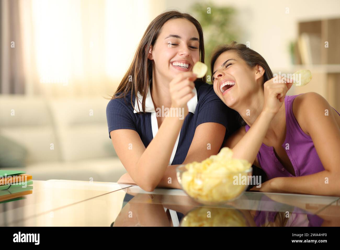Two funny roommates laughing and eating potato chips at home Stock Photo