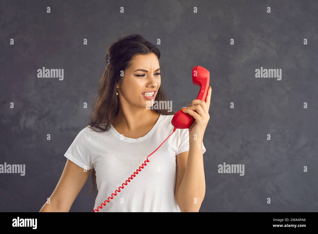 Frustrated woman standing on gray background reacts negatively to phone conversation. Stock Photo