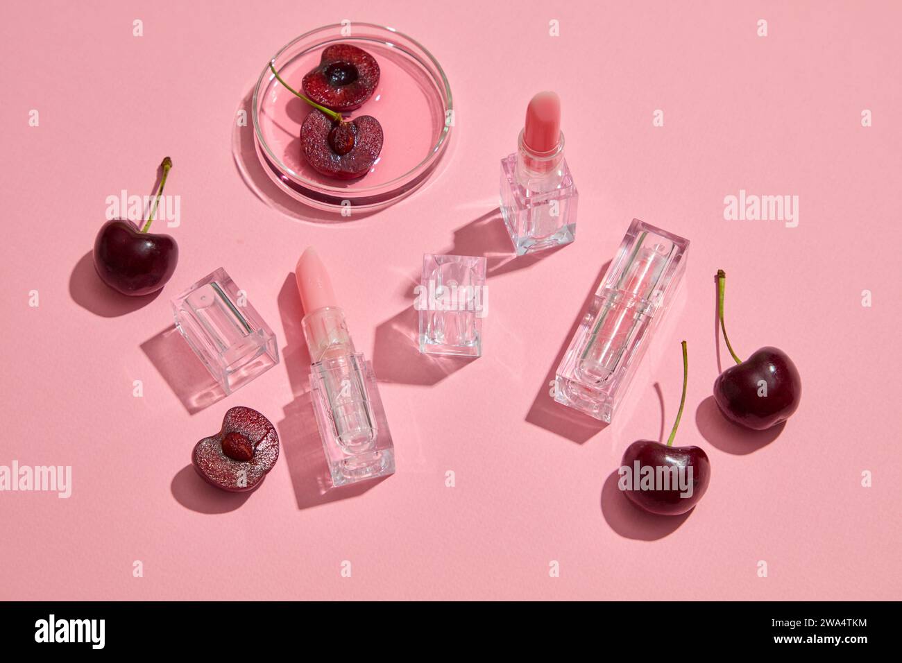 Against the pink background, cute lipsticks with transparent outer shell decorated with fresh cherries. Cherry red is a very popular lipstick color lo Stock Photo