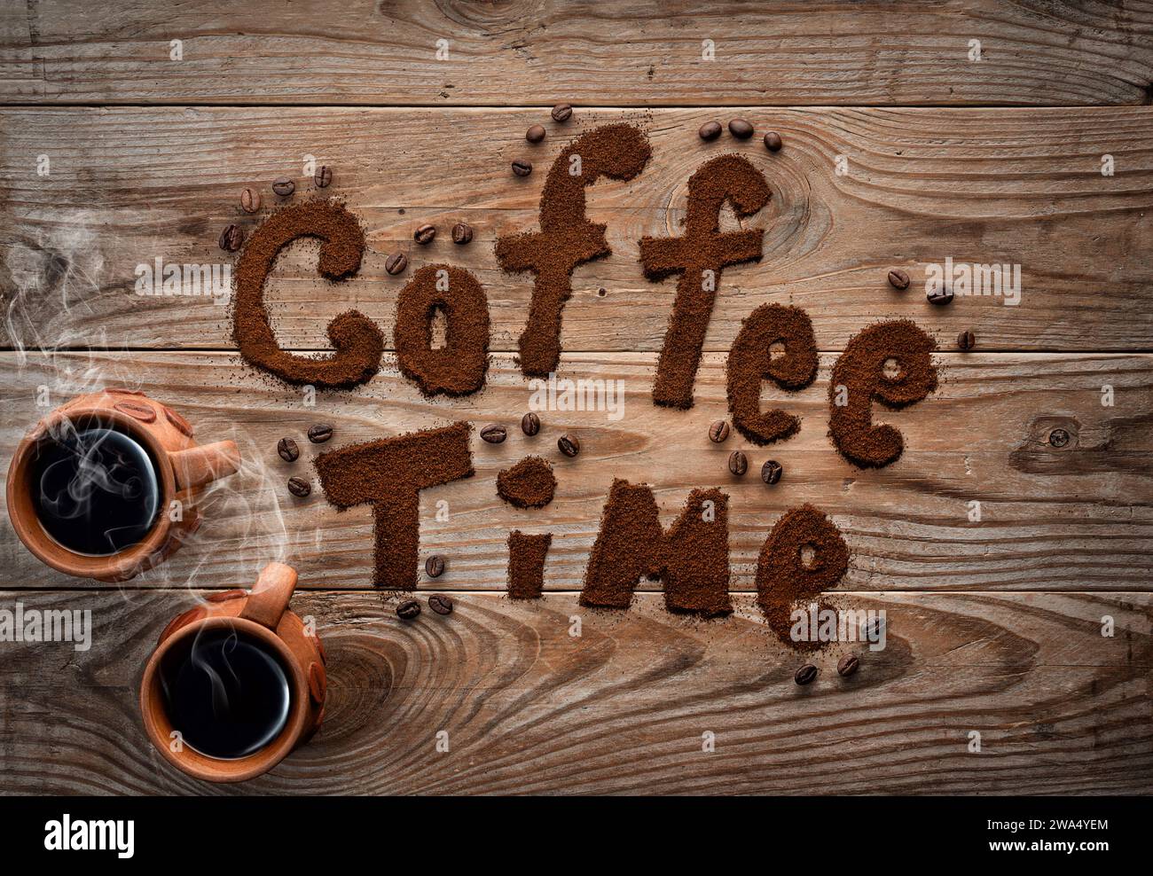 Coffee time written by ground coffee on textured wooden background. Two cups with hot coffee with steam. Stock Photo