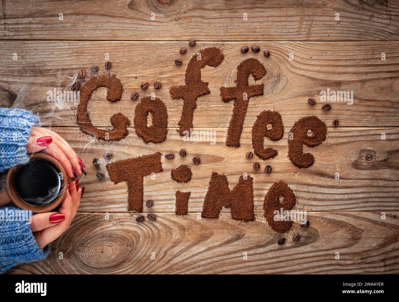 Coffee time written by ground coffee on a wooden background. Girl holding a cup of coffee with steam. Stock Photo