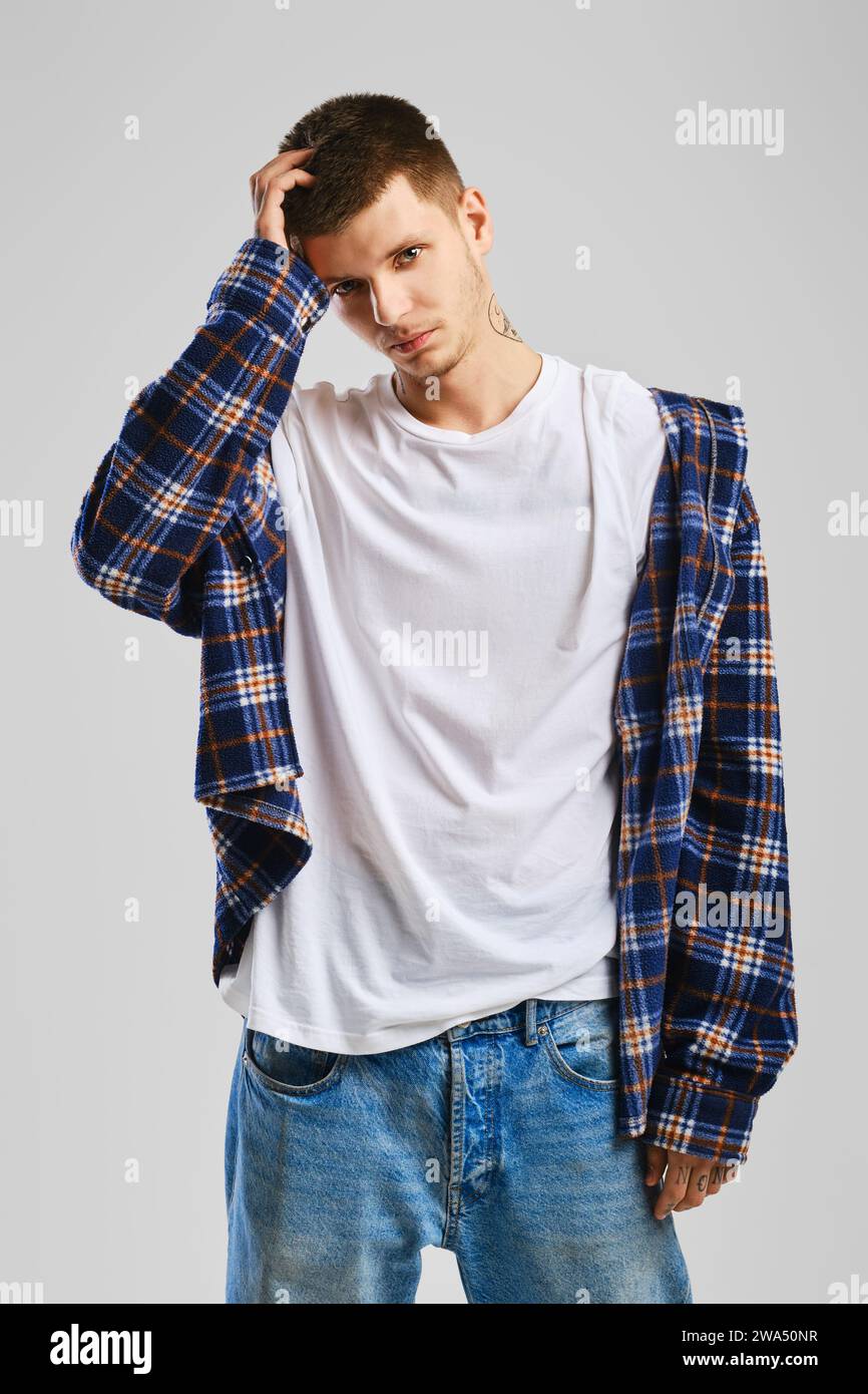 Young cocky man in checkered shirt and jeans touching his head Stock Photo