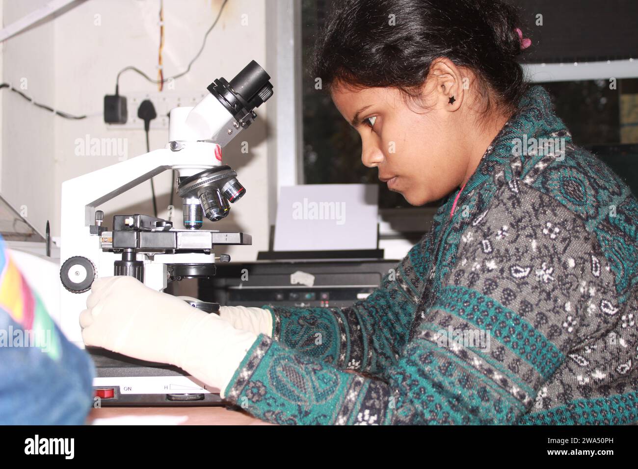 Lady pathologist examining with microscope. India Stock Photo