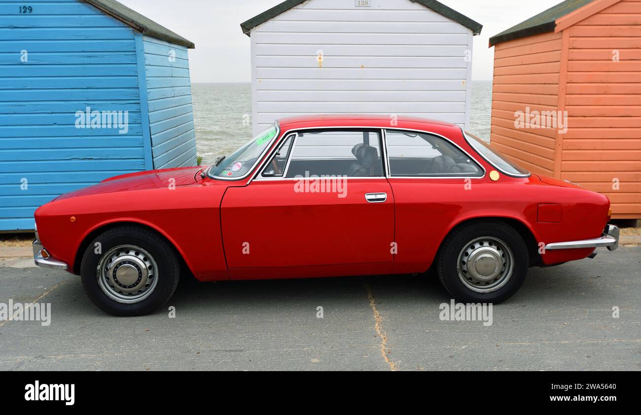 Classic Red Alfa Romeo Motor Car Parked in front of Beach Hut on seafront promenade Stock Photo