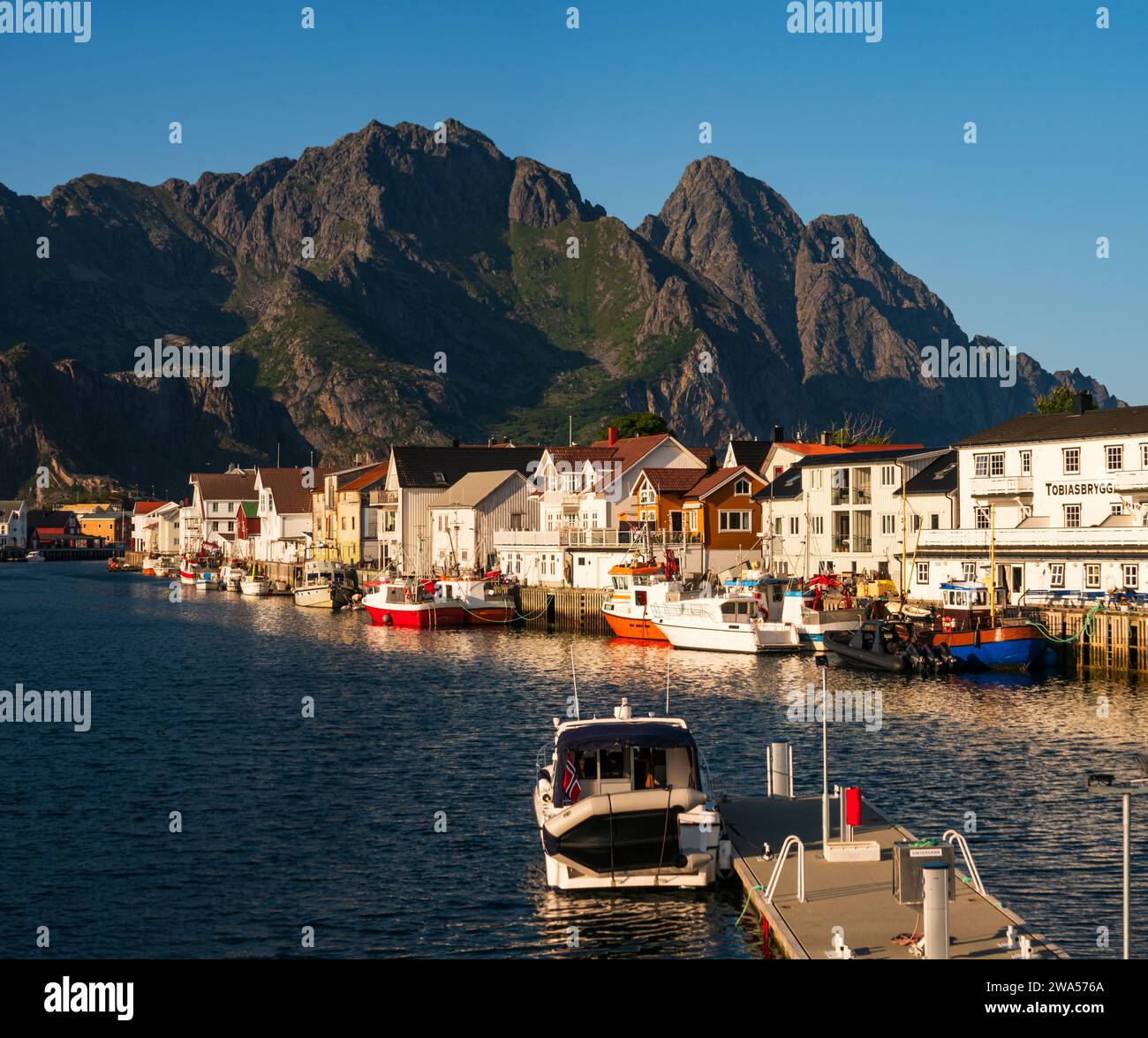 The small village of Henningsvaer on the southern coast of Lofoten, on a bright summer evening, fishing boats and sailboats alongside colorful houses. Stock Photo