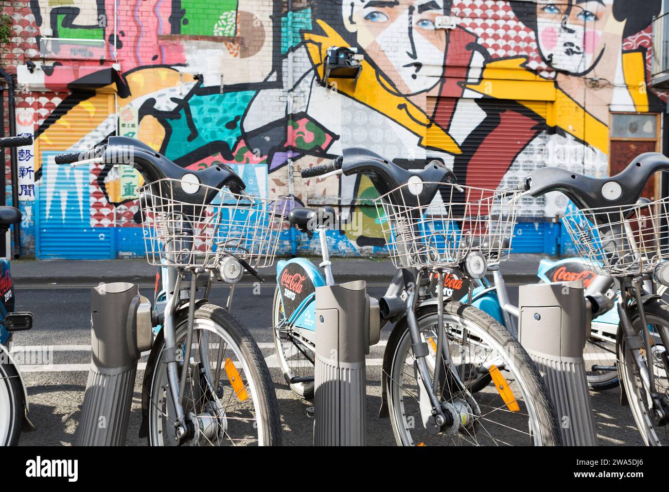 Ireland, Dublin, hire bikes in their cycle rack and wall graffiti in the Temple Bar area. Stock Photo