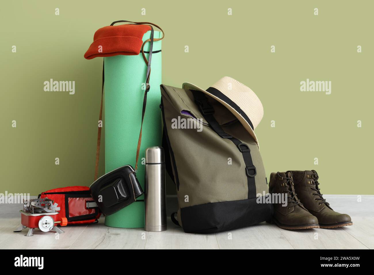 Set of camping equipment with backpack, portable stove, thermos and boots near green wall Stock Photo
