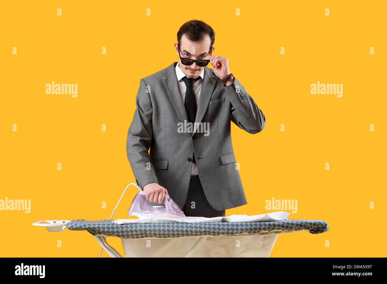 Young businessman ironing shirt on board against yellow background