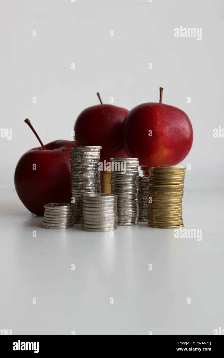 Columns of coins in front of red apples as an illustration of seasonal fruits cost Stock Photo