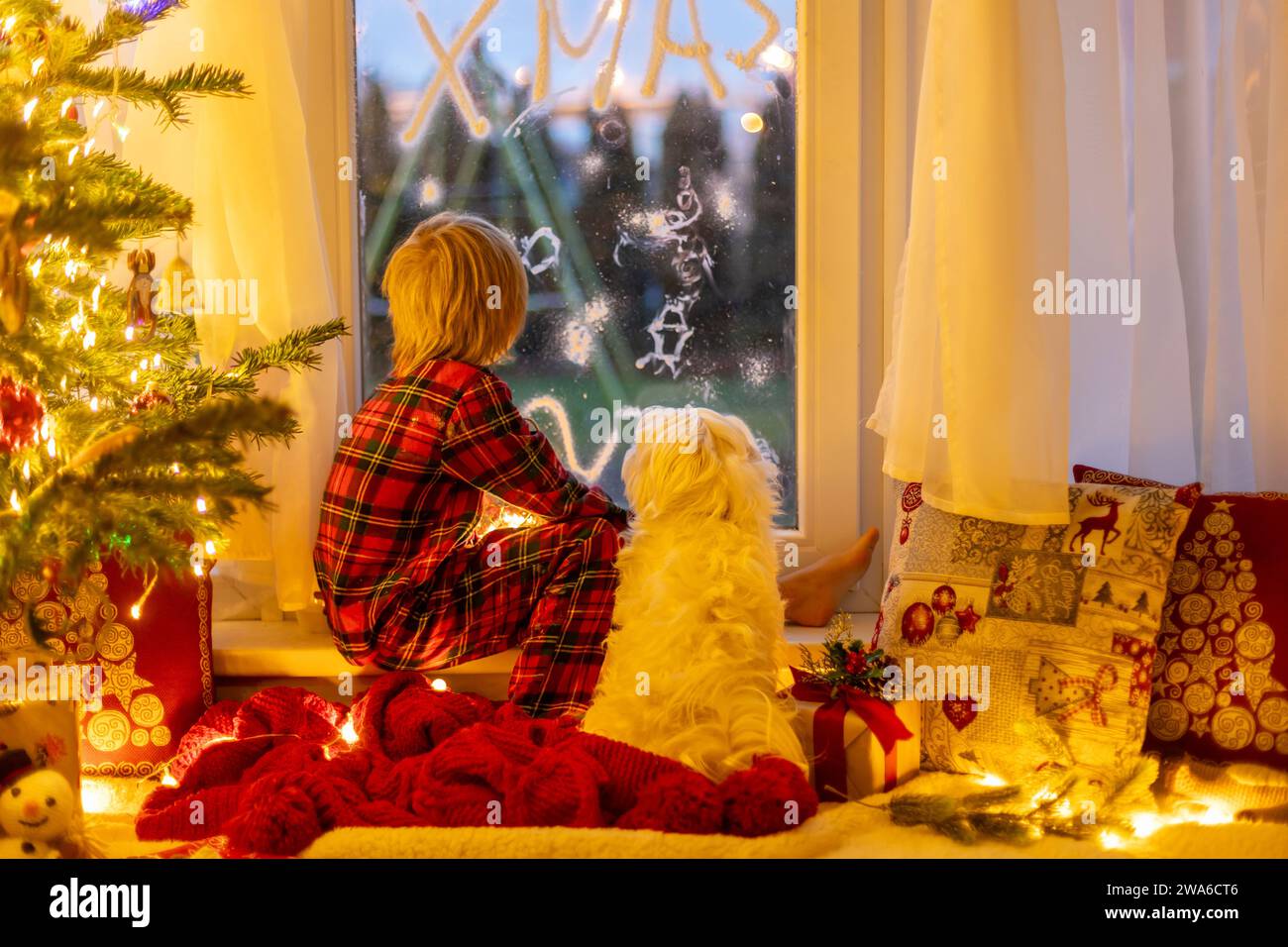 Cute child, sitting on a window, looking outdoors for Santa Claus, eating cookies Stock Photo