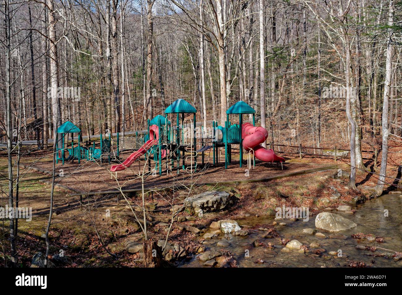 Large colorful playground equipment with slides and climbing towers alongside a creek in the woodlands in a park on a sunny day in wintertime Stock Photo