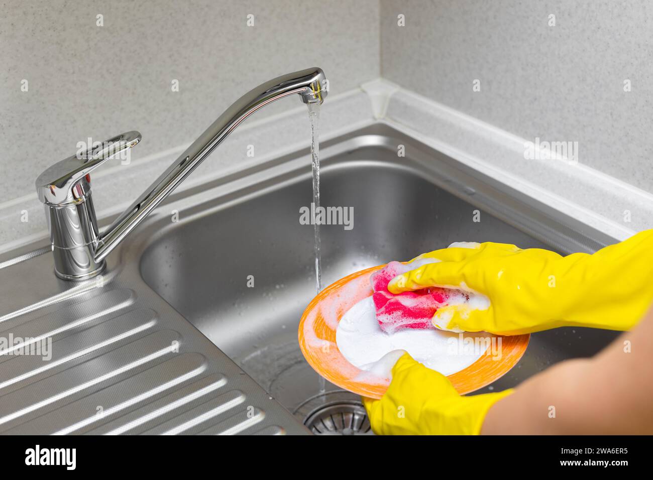 housewife in rubber gloves washes dishes in the kitchen. a woman in ...