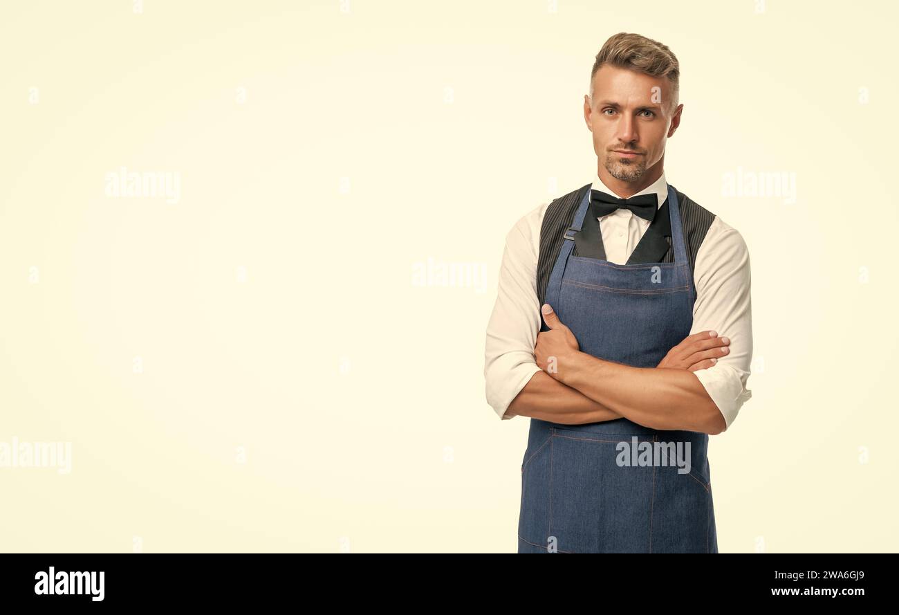 Confident serious guy in waiter apron and bow keeping arms crossed isolated on white, copy space. Stock Photo