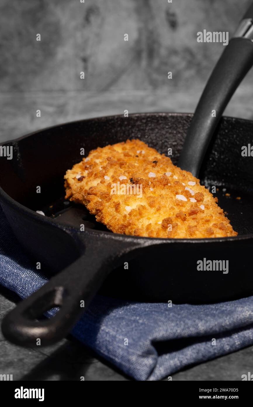 Pan fried breaded haddock fish in a cast iron frying pan. On a dark