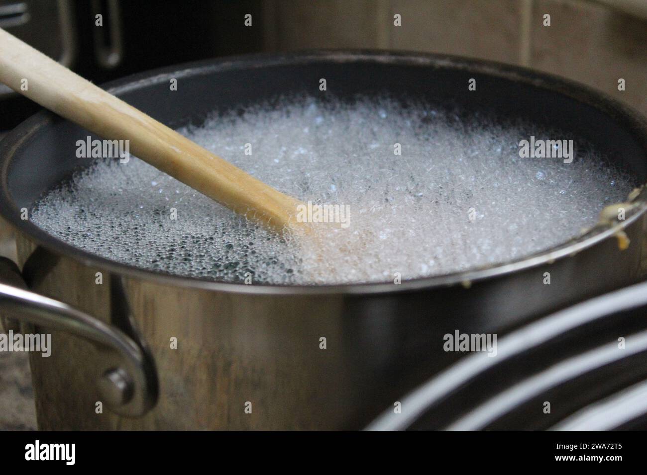 A close up photo of a wooden spoon in a kitchen pot full of suds and water. Stock Photo