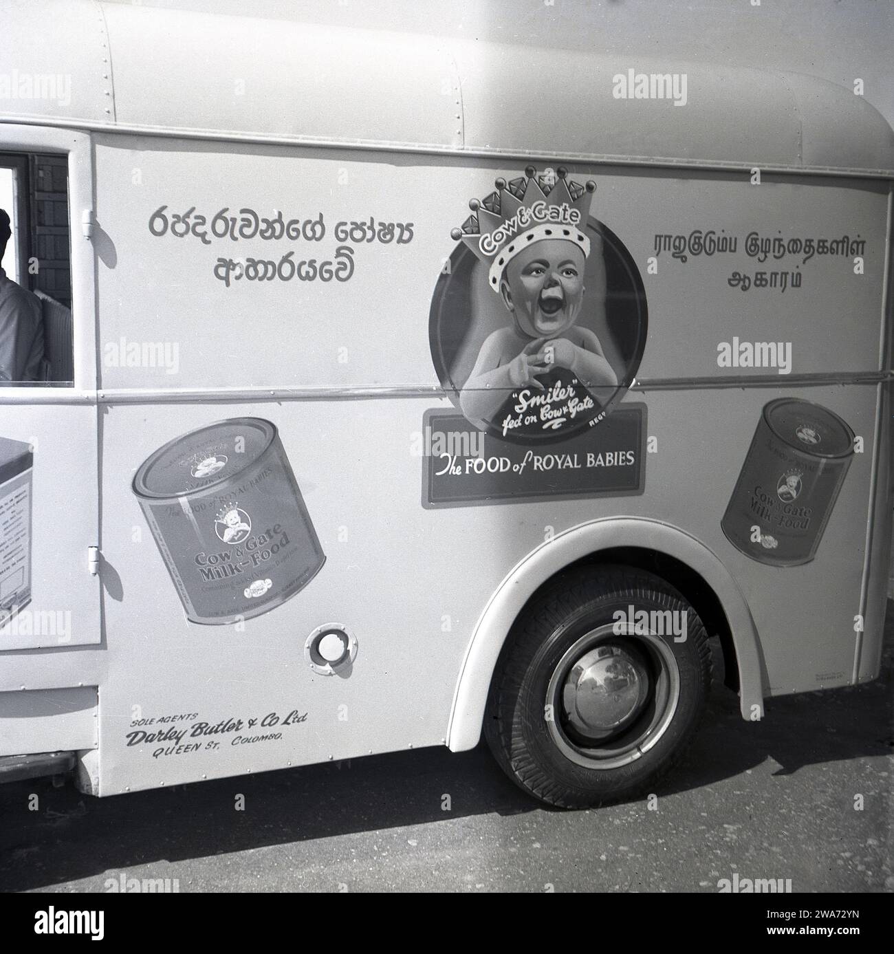 1953, historical, side view of a Commer delivery van on a road in Colombo, Celyon, showing a smiling baby wearing a crown with the strapline, 'the Food of Royal Babies' and tins of Cow & Gate Milk-Food. Sole Agents: Darley Butler & Co Ltd, Queen St, Colombo. The Cow & Gate 'smiler', a happy, healthy looking baby, first appeared on its product packaging & adverts in the 1930s. The 'Royal Baby; with a crown on its head dates back to 1937 and the Coronation of Briitsh King George VI, when the English diary company began to use 'royal association' to endorse their baby milk formula. Stock Photo