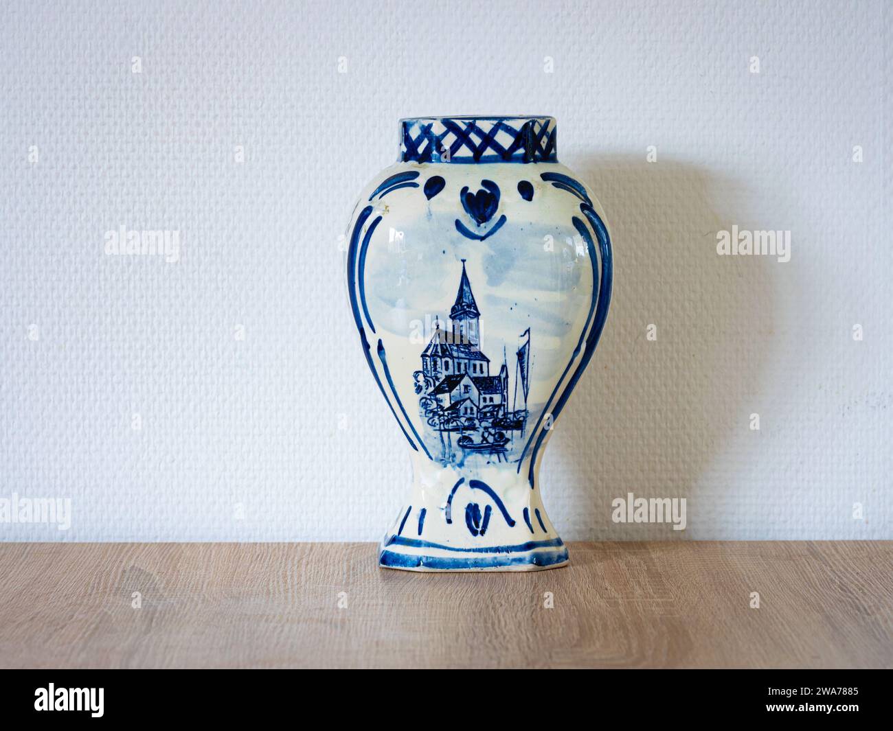 Delft blue ceramic vase with a pictured picturesque church on a table. The vase is made of porcelain and glazed on the outside. Stock Photo