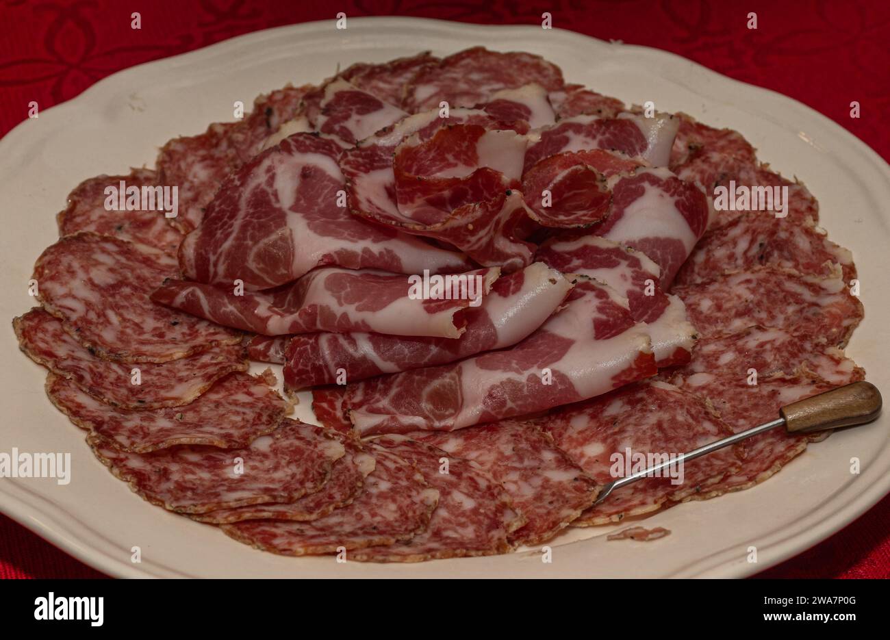 Sliced Salami and Soppressata Arranged on White Plate over Red Tablecloth Stock Photo