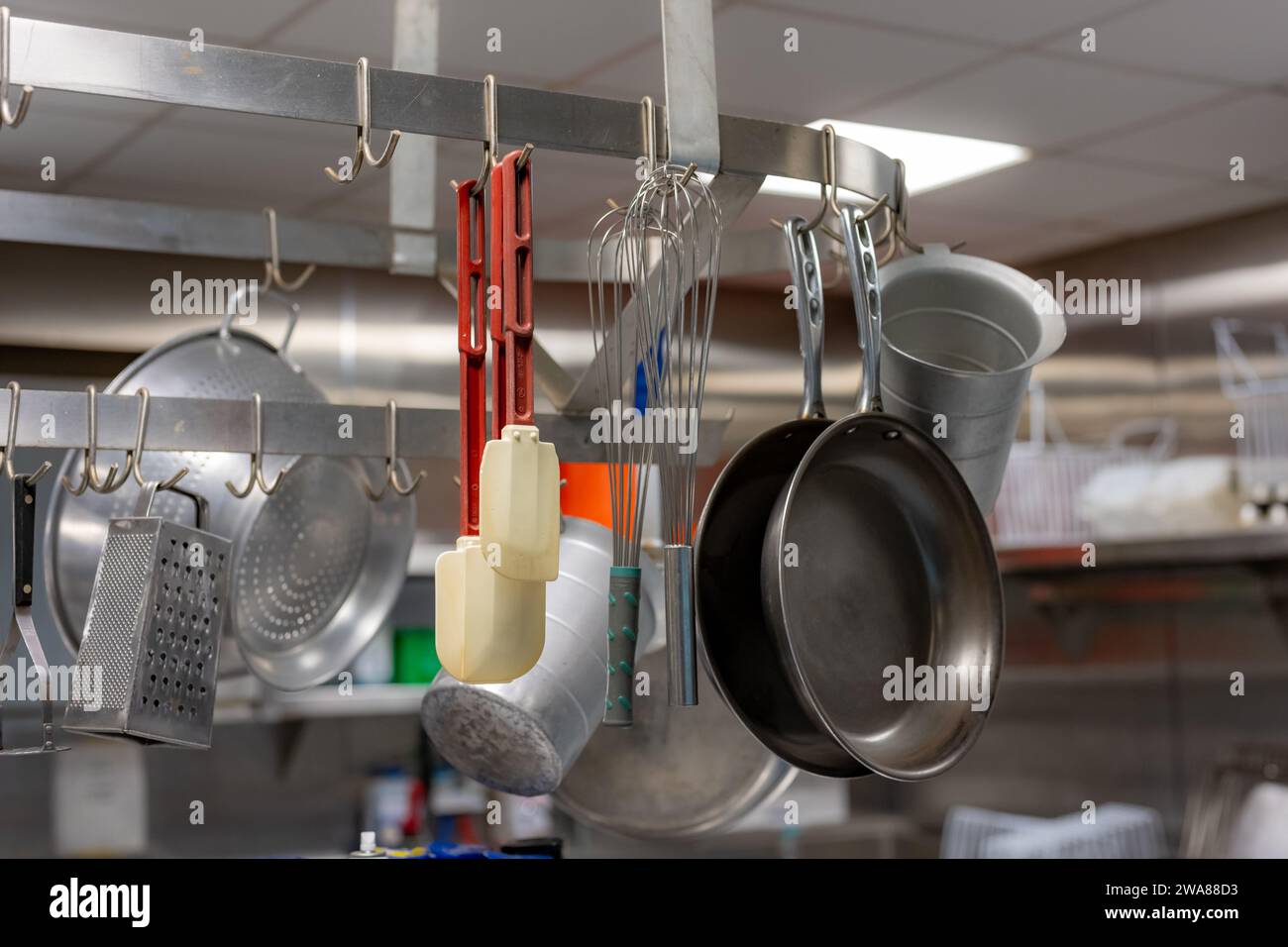 Stainless steel pots and pans and other cooking utensils hanging in a commercial industrial kitchen. Stock Photo