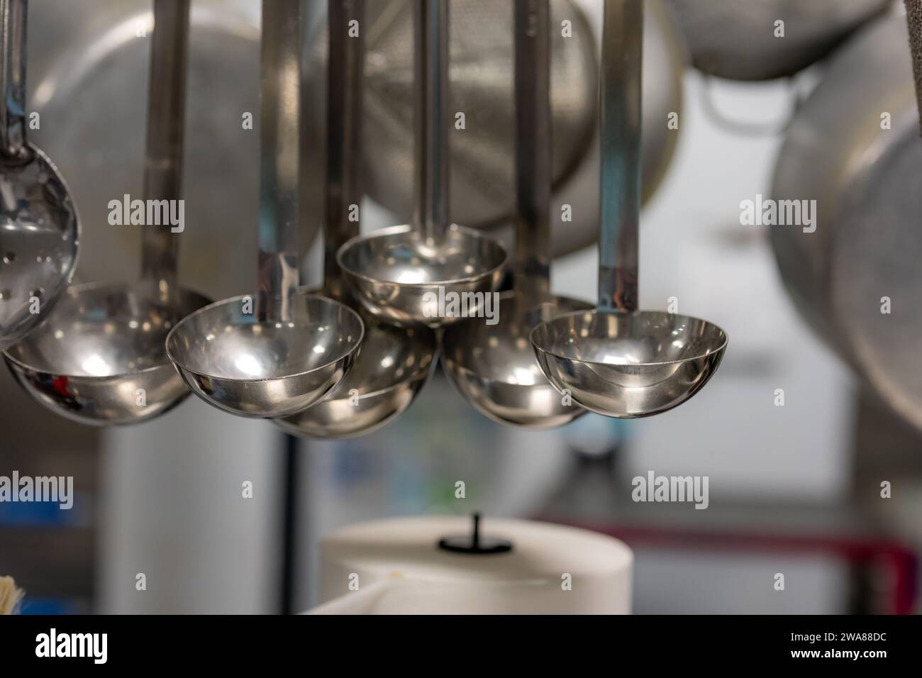 Stainless steel cooking utensils hanging in a commercial industrial kitchen. Stock Photo