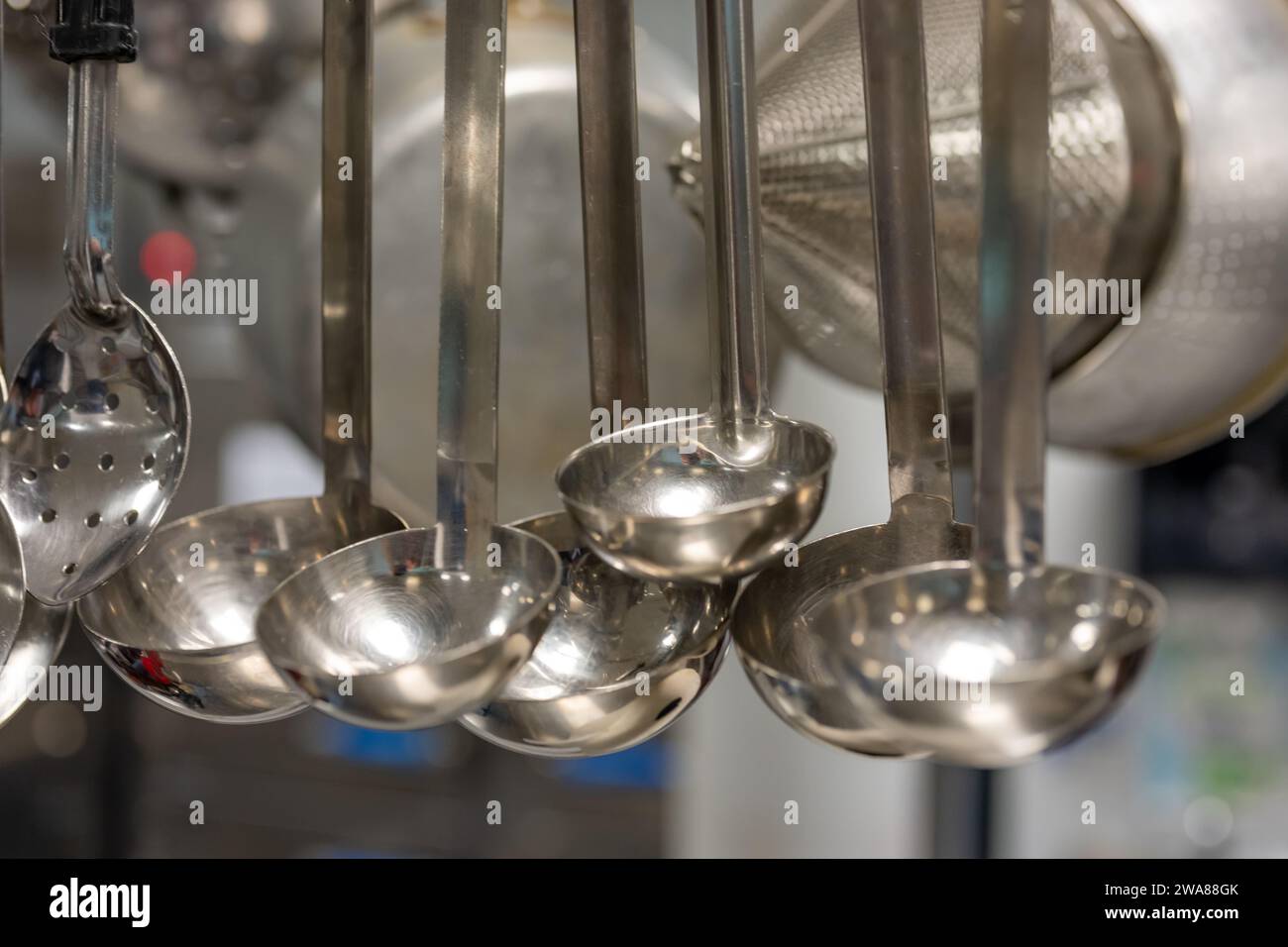 Stainless steel cooking utensils hanging in a commercial industrial kitchen. Stock Photo