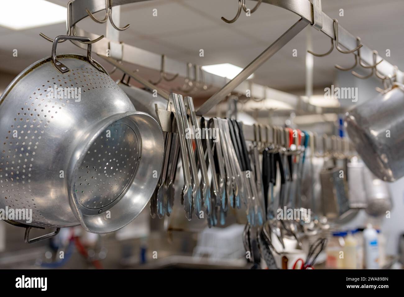 Stainless steel pots and pans and other cooking utensils hanging in a commercial industrial kitchen. Stock Photo