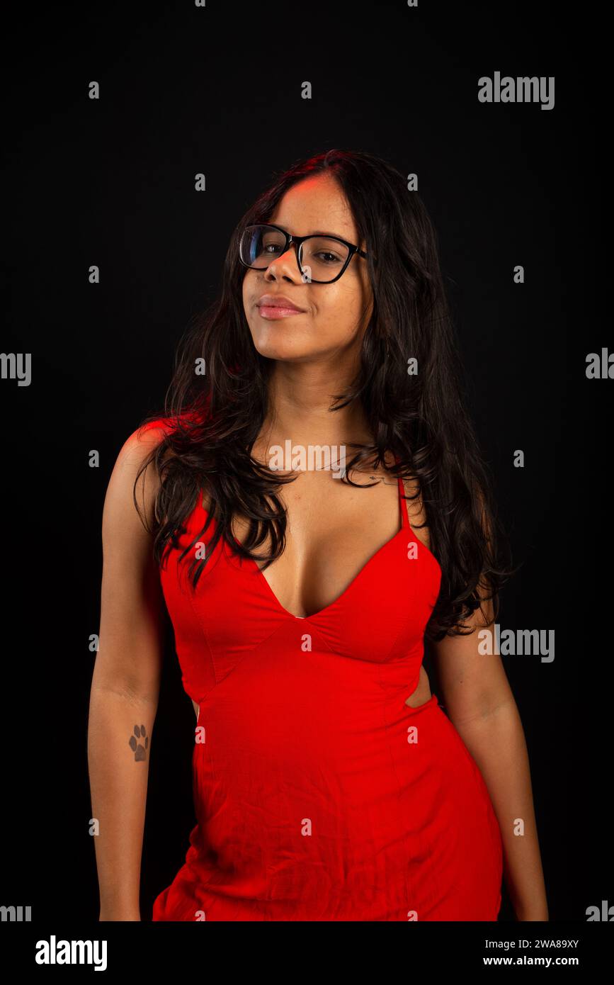 Beautiful young woman with straight hair wearing glasses and red dress. Isolated on black background. Stock Photo