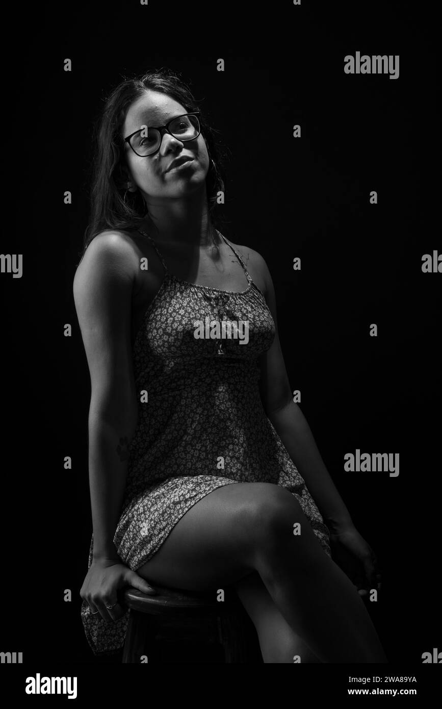 Black and white portrait of young woman with straight hair wearing glasses posing for photo. Stock Photo