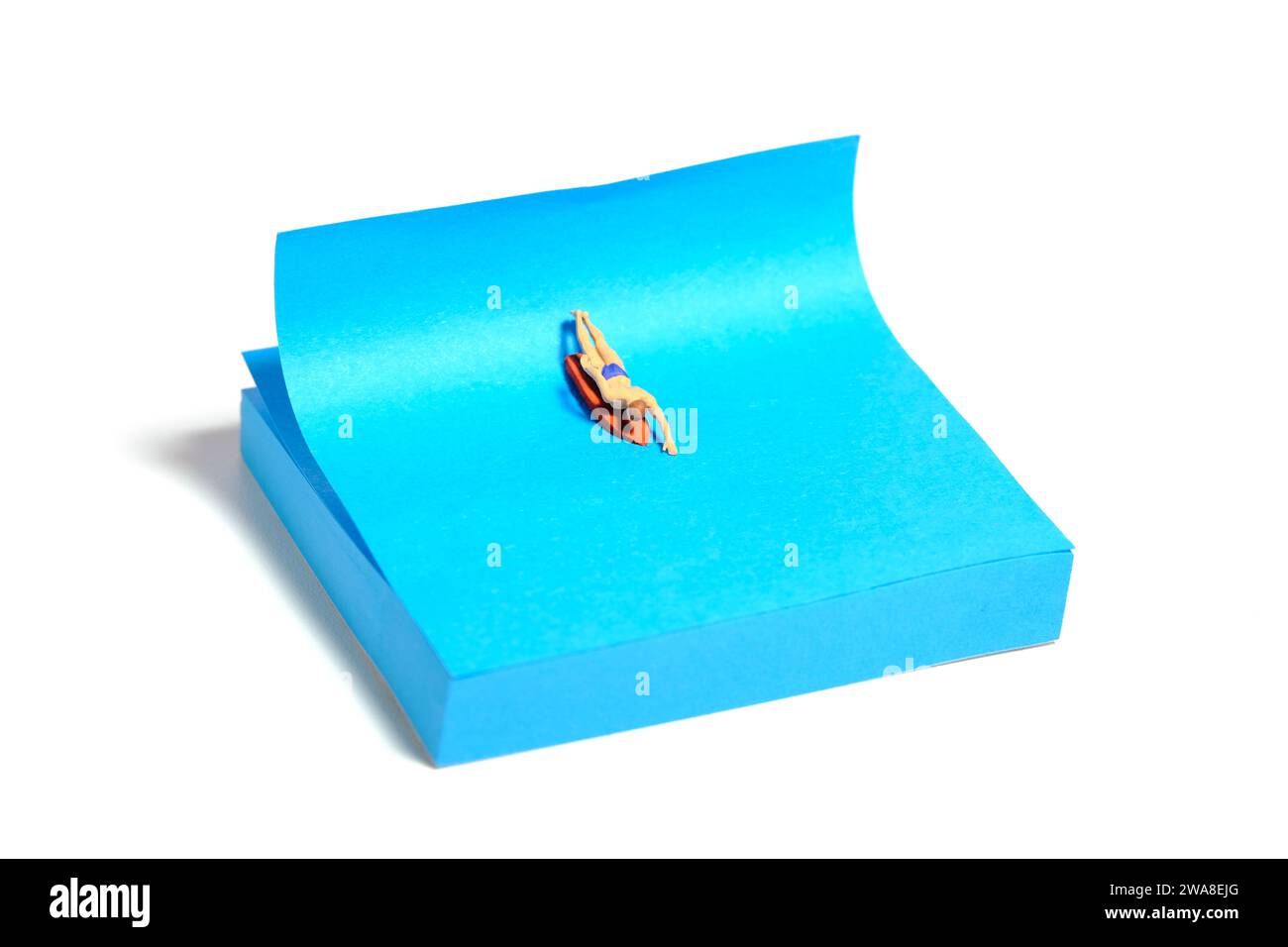 Creative miniature people toy figure photography. Sticky notes installation. A men surfer swimming above surfing board. Isolated on white background. Stock Photo