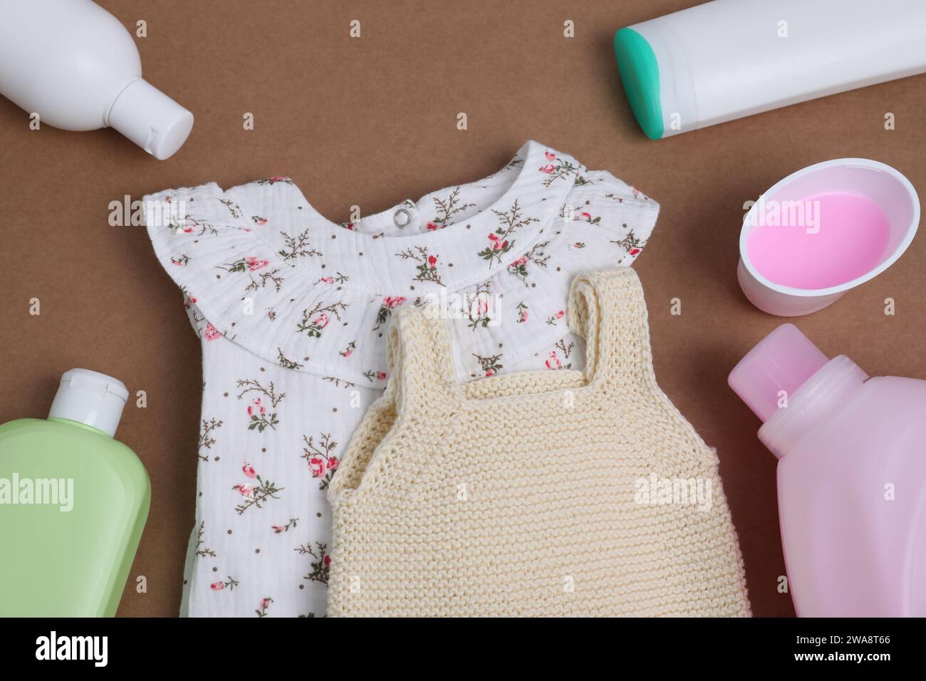 Laundry detergents and baby clothes on brown background, flat lay Stock