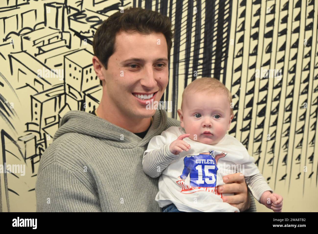 Hawthorne, United States. 02nd Jan, 2024. Tommy DeVito (L) holds a baby wearing a New York Giants shirt with 'Cutlets' written on it. Tommy DeVito participates in an autograph signing and meet and greet at Bogie's Hoagies and Deli in Hawthorne. Thomas N. DeVito is an American football quarterback for the New York Giants of the National Football League. Credit: SOPA Images Limited/Alamy Live News Stock Photo
