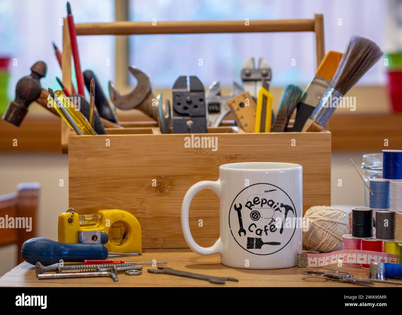 Repair Cafe logo on a cup surrounded by repair tools on table in café used as a repair centre, consumer activism to repair household items Stock Photo