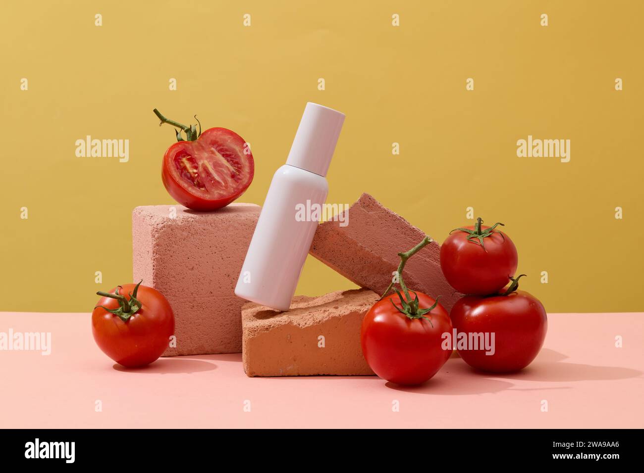 A skin care bottle with empty label arranged on several stones with red tomatoes. Yellow background. Tomatoes are low in calories and full of vital nu Stock Photo