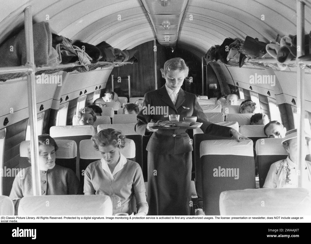 Airline travelling in the 1950s. A group of women and  men on an swedish passenger airplane in the 1950s. The female flight attendant is standing in the middle of the airplane serving coffee and sandwiches to the passengers. Sweden 1957 Stock Photo