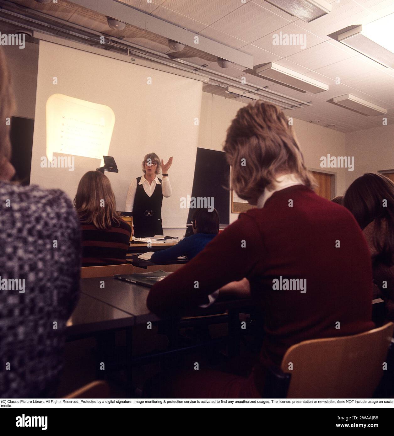 In the 1970s. A school class sits in the benches during a lesson with a