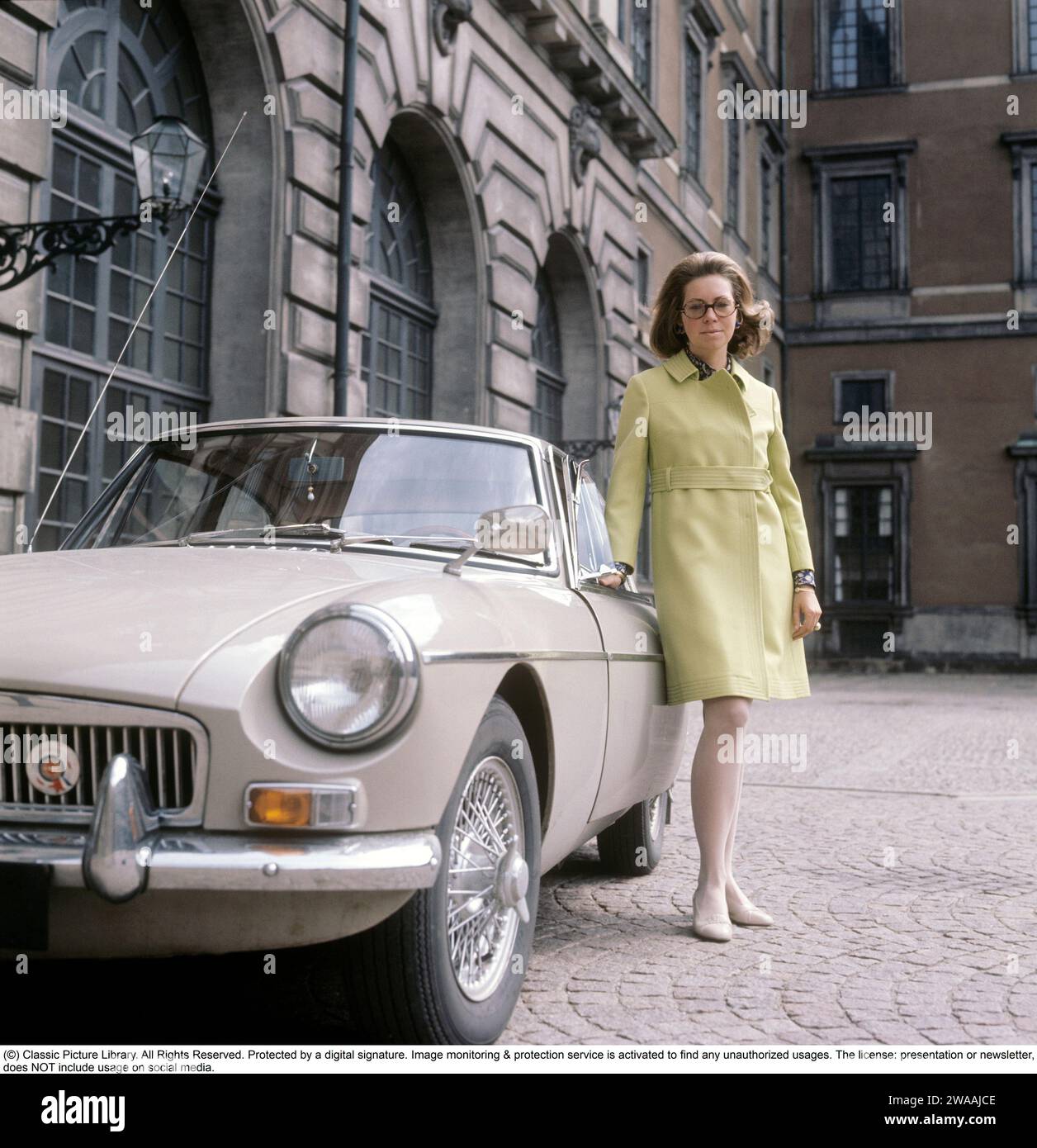 Princess Christina, Mrs. Magnuson. Sister of Sweden's King Carl XVI Gustaf. Born on 3 August 1943.   The car that is two years old here is an MG MGB, a sports car in the color Sany Beige, produced by the British car manufacturer MG between 1962 and 1980. It was available as a convertible and with a 2+2-seater covered body (GT). The six-cylinder versions produced from 1967-69 were called MGC. Photographed outside the Royal Palace in Stockholm on June 2, 1969 in a period outfit. Stock Photo